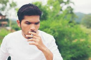 Young hipster man taking rest, smoking cigarette with nature and fresh breeze. photo