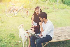 una joven pareja de educación sentada en el banco juega con un perro al aire libre y hace buen tiempo. y son felices, concepto de estilo de vida. foto