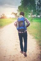 Close up young hipster man with backpack on his shoulder walking down countryside.