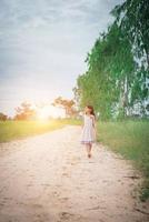Little girl wearing dress is walking and look away from down rural road. photo