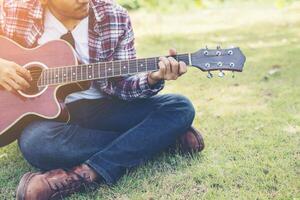 Young hipster man practiced guitar in the park,happy and enjoy playing guitar. photo