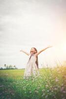 linda niña asiática de pie entre el día de sol del campo de flores púrpura. libertad disfrutando con la naturaleza. foto