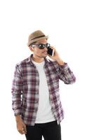 Handsome hipster young man in hat and sunglasses standing and talking on mobile phone over white background. photo