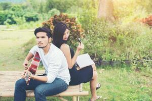joven pareja encantadora enamorada tocando guitarra acústica en el parque. relajándose con la naturaleza, concepto de estilo de vida. foto