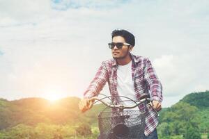 un joven hipster montando en bicicleta hasta la cima de la montaña disfruta de la brisa fresca y la naturaleza detrás de la vista de la montaña. foto