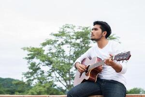 Young hipster man playing guitar to relaxing on his holiday, enjoy with natural and fresh air. photo