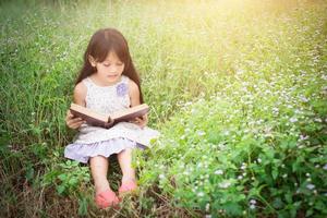 linda niña asiática leyendo un libro en la naturaleza. foto