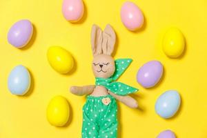 Happy Easter concept. Preparation for holiday. Colorful decorated easter eggs and bunny toy isolated on trendy yellow background. Simple minimalism flat lay top view, copy space photo