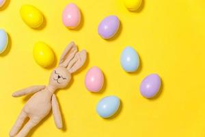 Happy Easter concept. Preparation for holiday. Colorful decorated easter eggs and bunny toy isolated on trendy yellow background. Simple minimalism flat lay top view, copy space photo
