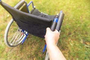 Hand holding empty wheelchair in hospital park waiting for patient services. Wheel chair for person with disability parked outdoor. Accessible for person with disability. Health care medical concept. photo