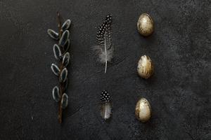 Happy Easter concept. Preparation for holiday. Golden decorated easter eggs willow feather on trendy grunge scratched dark black shale background. Simple minimalism flat lay top view, copy space photo