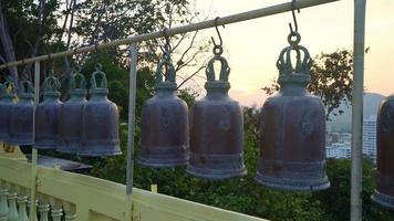 campane metalliche appese in fila fuori nel tempio buddista tailandese, campana del tempio tailandese che credono che chi bussa a questa campana avrà la fortuna video