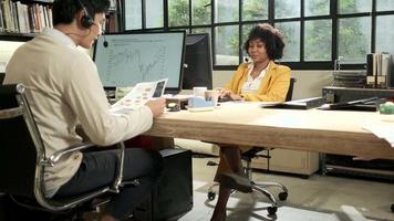 Two staff and coworkers, African American female worker and Asian male colleagues working and talking with a communication headset to contact a business, customer support in the open workplace office. video