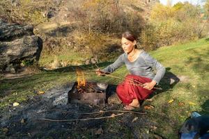 Woman with Indian red pants is making bonfire in the forest to cook photo