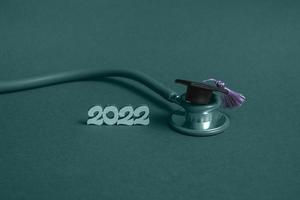 Graduation cap with stethoscope and numbers 2022 on blue background, closeup with copy space. Medical education concept. photo