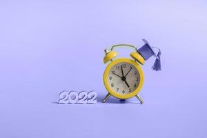 Yellow alarm clock with graduation cap on blue background closeup with copy space photo