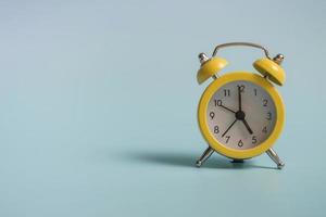 Yellow alarm clock with graduation cap on blue background closeup with copy space photo