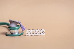 Graduation cap with stethoscope and numbers 2022 on beige background, closeup with copy space. Medical education concept. photo