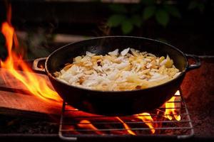 Potatoes fried in a pan on a fire with onions. Delicious food in nature. photo