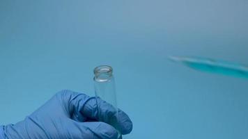primer plano artístico de dos frascos médicos de vidrio que vierten líquido médico azul de uno a otro en un laboratorio moderno con un fondo azul. el concepto de investigación y desarrollo. video