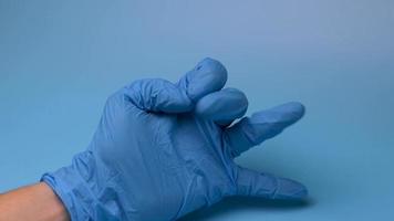 une main dans un gant médical compte jusqu'à cinq sur fond bleu.