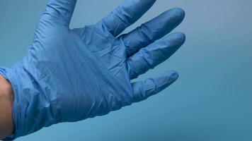 A hand in a medical glove counts to five on a blue background. video