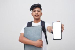 Young indian student holding file and showing smartphone screen on white background. photo