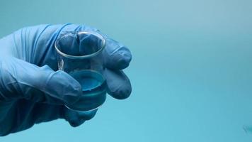 primer plano artístico de dos frascos médicos de vidrio que vierten líquido médico azul de uno a otro en un laboratorio moderno con fondo azul video