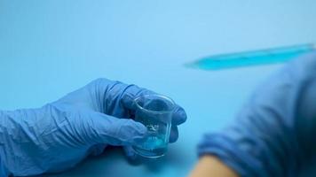 close-up artístico de dois frascos médicos de vidro derramando líquido médico azul de um para o outro em um laboratório moderno com fundo azul. o conceito de pesquisa e desenvolvimento. video