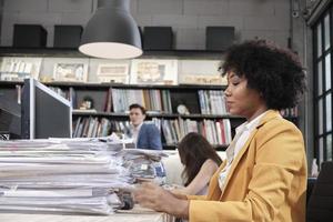 trabajadora ocupada, el personal afroamericano joven está trabajando duro con una gran cantidad de documentos y papeleo en el escritorio, la sobrecarga trabajó incansablemente para la fecha límite del trabajo en el espacio de trabajo de la oficina comercial. foto