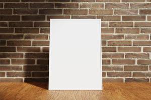 Vertical white poster or photo frame mockup on the wooden table with blurry brick background