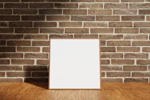 Square wooden poster or photo frame mockup on the wooden table with blurry brick background