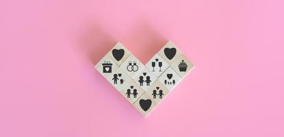 el amor es y el concepto del día de san valentín. los bloques de madera del cubo están dispuestos en forma de corazón con íconos como familia, amante de las mascotas, lgbtq, anillo, champán y regalo sobre fondo rosa. foto