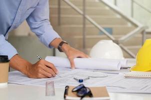 The engineer is drafting the planning structure. with architect equipment and architectural blueprints at the desk, coffee photo