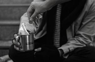 primer plano de los pobres o personas sin hogar personas sin hogar piden dinero en público. el pobre mendigo de la ciudad se sentó en las escaleras con una taza de plata. foto