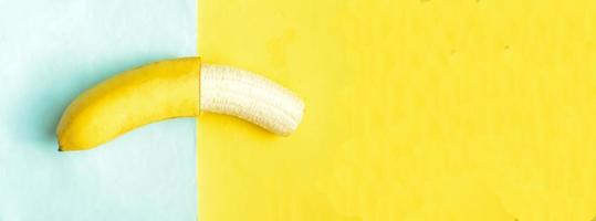 One partially peeled banana on blue yellow background, photo