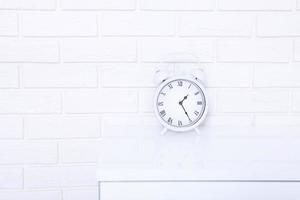 Retro alarm clock with twenty five minutes past one o'clock near brick wall on white workplace. Selective focus photo