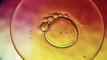 óleo de comida colorido abstrato deixa cair bolhas e esferas fluindo na superfície da água, macro videografia
