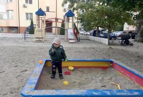 Beautiful baby in child sandpit posing photographer near sandbox photo