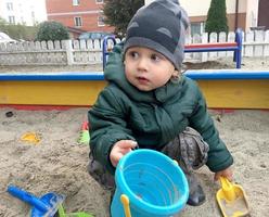 Beautiful baby in child sandpit posing photographer near sandbox photo