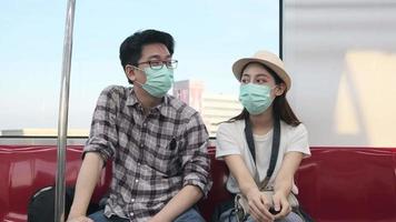 Young Asian couple tourist with face mask sitting in the passenger cabin of sky train, COVID-19 new normal travel with Thailand urban view, public railway transport, happy lifestyle journey vacation. video