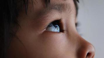 närbild porträtt av litet asiatiskt barn tittar upp i himlen. vackra bruna ögon, långa ögonfransar. video