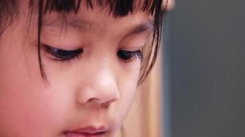 närbild porträtt av litet asiatiskt barn som läser en bok inomhus. vackra bruna ögon, långa ögonfransar. video