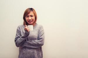 beautiful young woman holding a cup of coffee standing in her house and smiling to camera on the white background photo