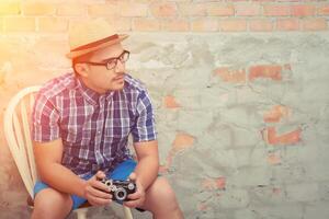 un apuesto hombre hipster sosteniendo una cámara retro en el fondo de ladrillo foto