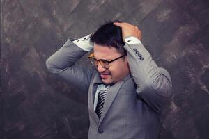 Terrible headache. businessman wearing glasses keeping eyes closed while standing against  beige brick background photo