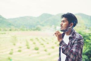 Hipster man smoking cigarette, standing behind a mountain. Among the fresh air in the morning. photo