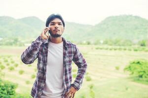 joven hipster barbudo hablando por teléfono, sonriendo, fuera de la vista a la montaña. foto