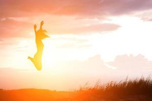 mujer feliz saltando contra la hermosa puesta de sol foto