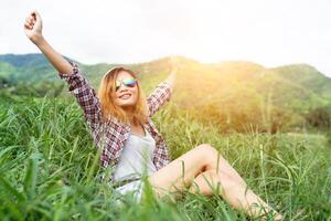 Beautiful hipster woman sitting in a meadow with nature and mountains in the background. photo